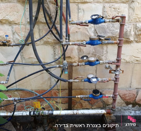 מד מים כחולים וצינורות מחוברים לקיר אבן